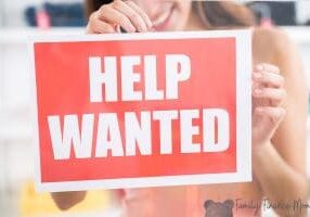 Midsection of smiling female owner holding help wanted sign in retail store